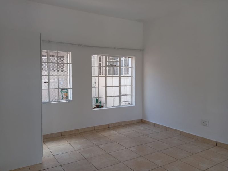 A bright, empty bedroom featuring tiled flooring, built-in cupboard storage, and windows fitted with security bars.