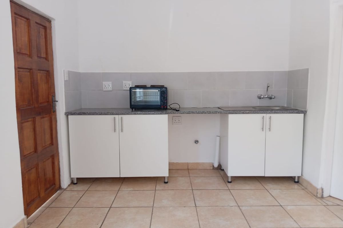 A compact kitchen area featuring white cabinetry, a granite countertop, a stainless steel sink, and tiled flooring, currently awaiting final finishes.