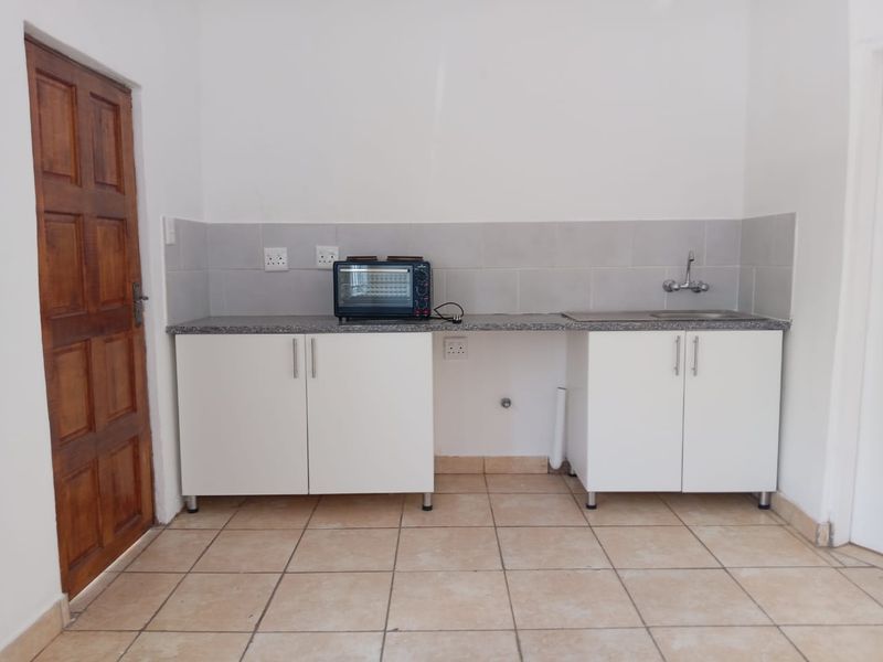 A compact kitchen area featuring white cabinetry, a granite countertop, a stainless steel sink, and tiled flooring, currently awaiting final finishes.