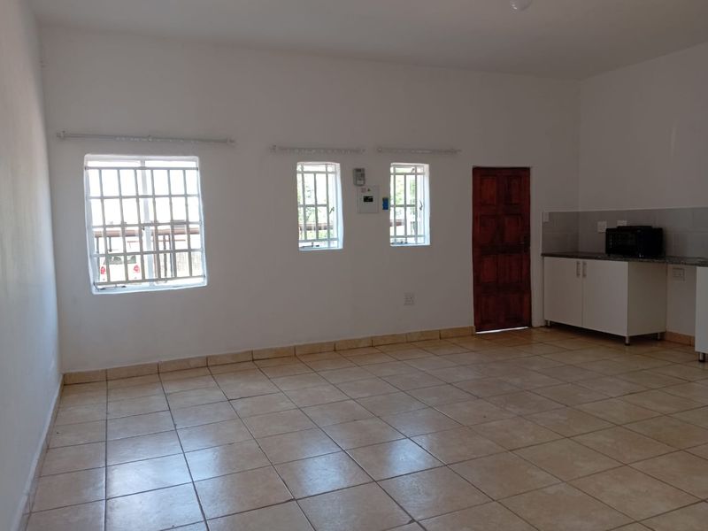 An open-plan living and kitchen area featuring tiled flooring, security-barred windows, and basic built-in kitchen cabinetry with a stone countertop.