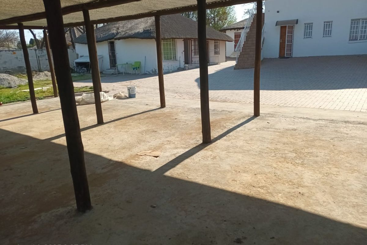 A spacious outdoor courtyard featuring a covered patio area with timber supports, paved ground, and access to an external staircase.