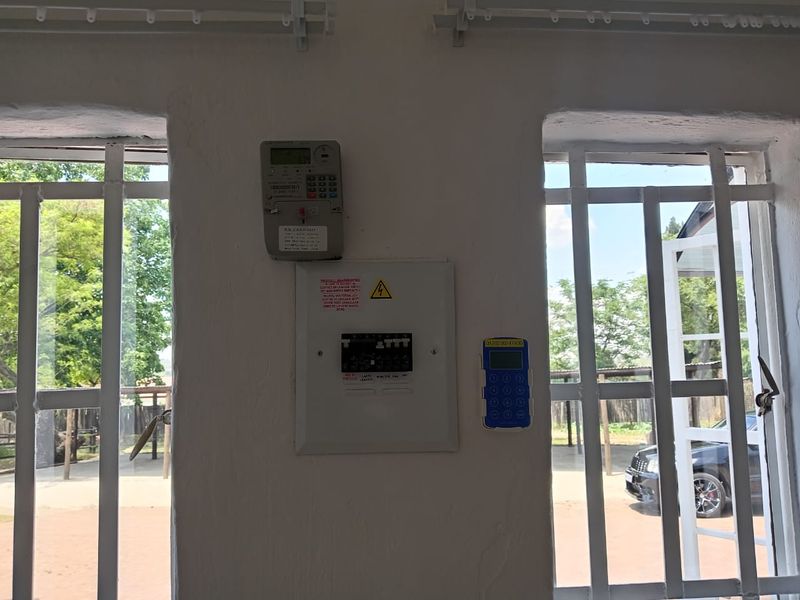Utility area featuring a wall-mounted electrical distribution board and prepaid electricity meter, positioned between two windows with security bars.
