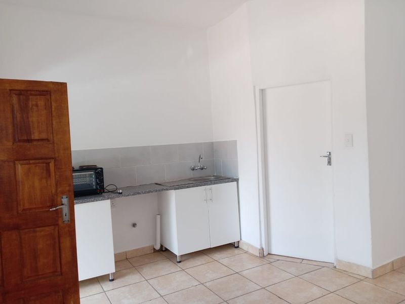 A compact kitchen area featuring white cabinetry, a granite countertop with a stainless steel sink, tiled backsplash, and ceramic floor tiles.
