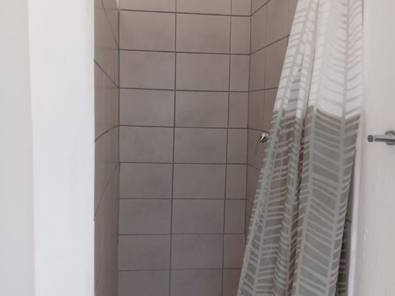A functional shower stall featuring neutral wall tiles, mosaic floor tiling, and a standard shower head fixture.