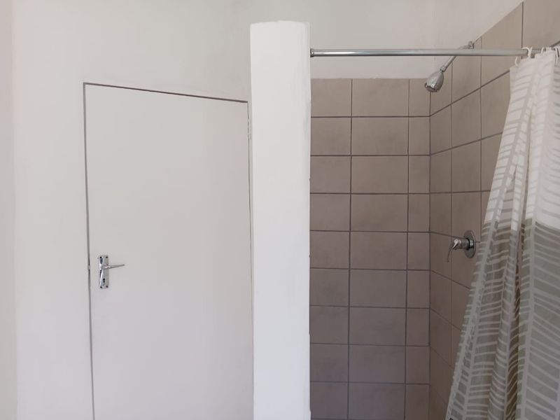 A functional bathroom featuring a tiled shower enclosure with a standard shower head and mixer, adjacent to an internal door.