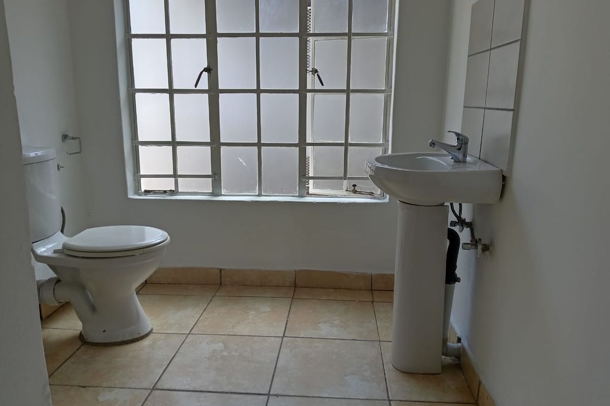 A functional bathroom featuring a pedestal basin, toilet, and tiled flooring, awaiting updates to modernize the space.