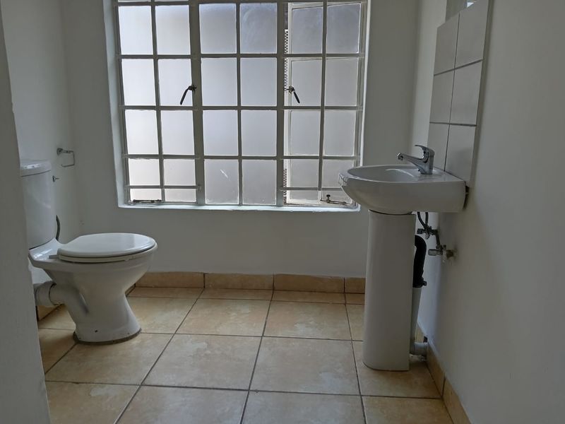 A functional bathroom featuring a pedestal basin, toilet, and tiled flooring, awaiting updates to modernize the space.