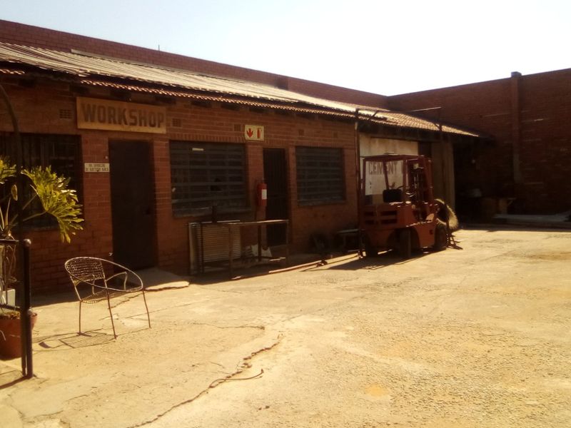 Industrial workshop exterior featuring a brick facade, corrugated metal roofing, and a spacious concrete yard area.