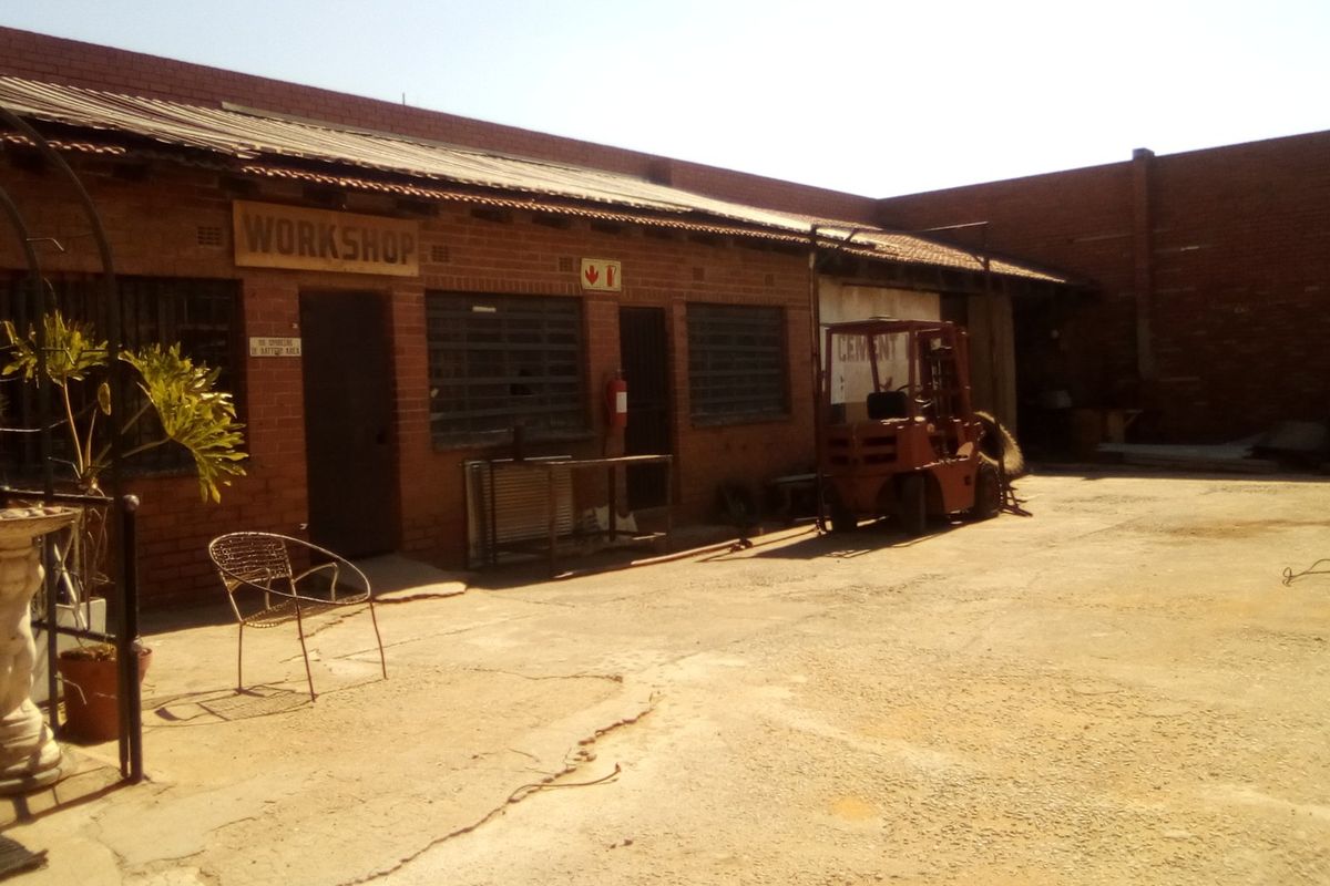 Industrial workshop exterior featuring a brick facade, corrugated metal roofing, and a spacious concrete yard area.