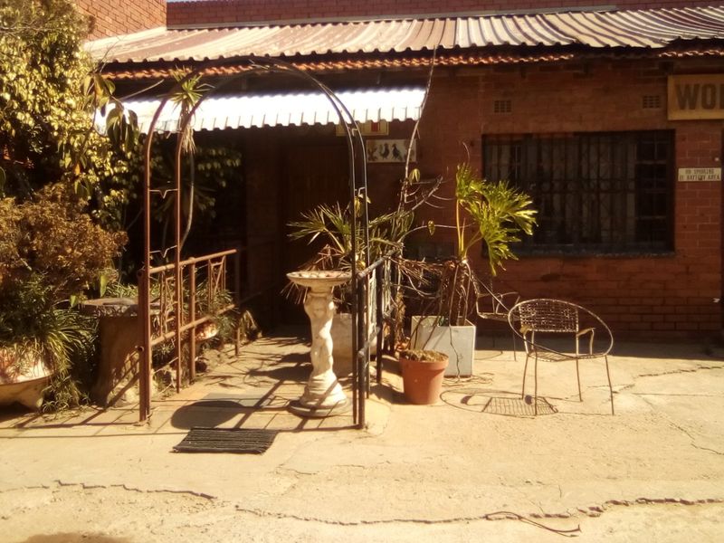 Front exterior view of an industrial workshop building featuring exposed brickwork, a corrugated metal roof, and concrete paving.