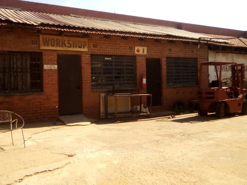 Industrial workshop exterior featuring a red brick facade, corrugated metal roofing, and a concrete apron, suitable for heavy-duty operational use.