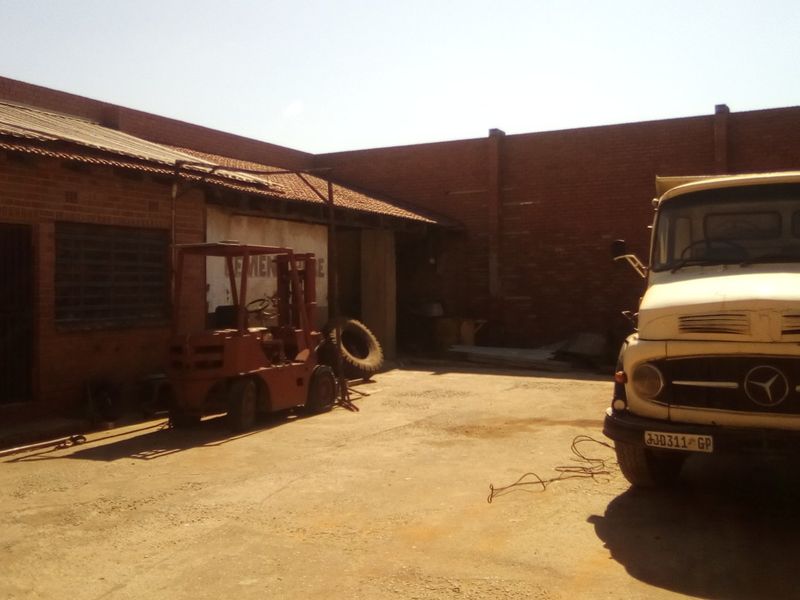 Industrial rear yard area featuring a concrete surface, brick perimeter walls, and a corrugated metal roof structure.