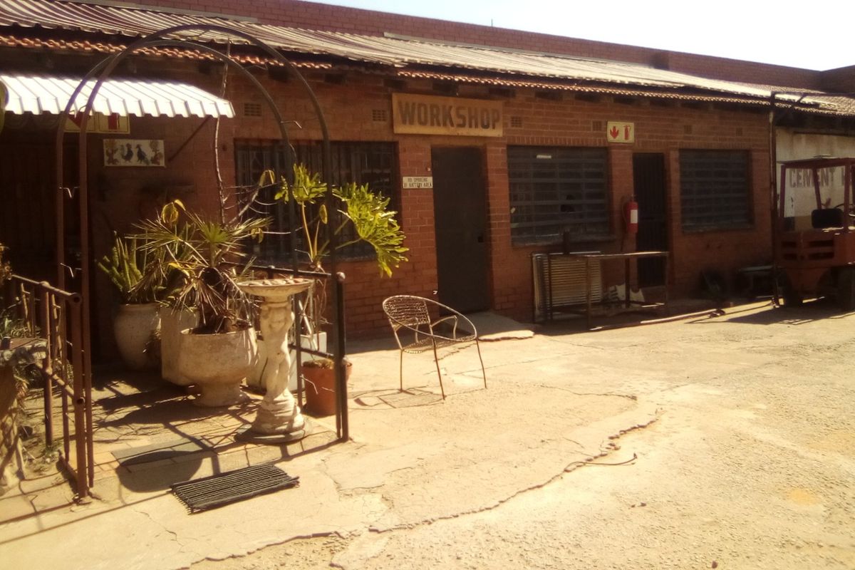 Exterior view of an industrial workshop building featuring exposed brick walls, security-barred windows, and a concrete yard area.