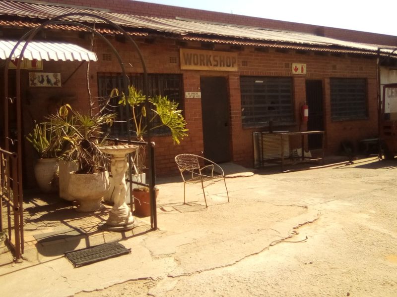 Exterior view of an industrial workshop building featuring exposed brick walls, security-barred windows, and a concrete yard area.