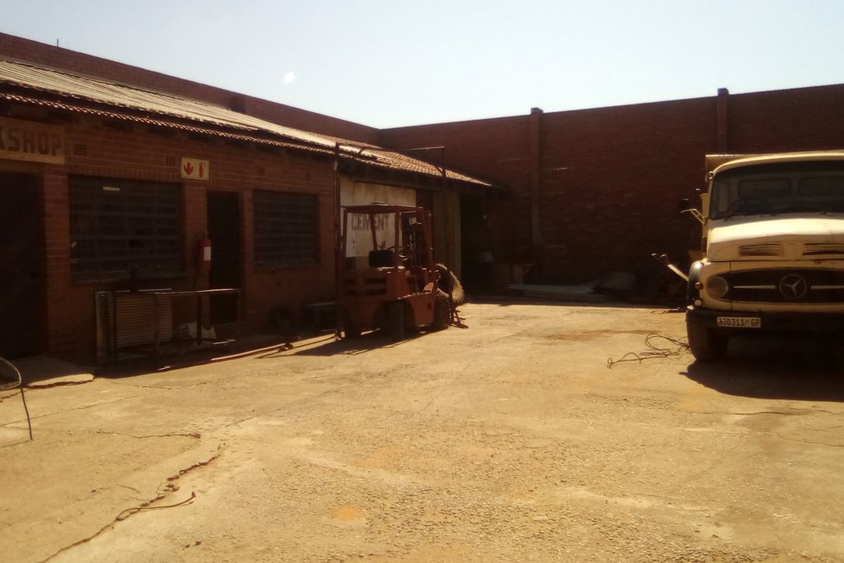 Industrial workshop exterior featuring a brick facade, corrugated metal roofing, and a spacious concrete yard area.