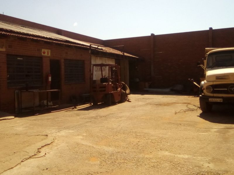 Industrial workshop exterior featuring a brick facade, corrugated metal roofing, and a spacious concrete yard area.