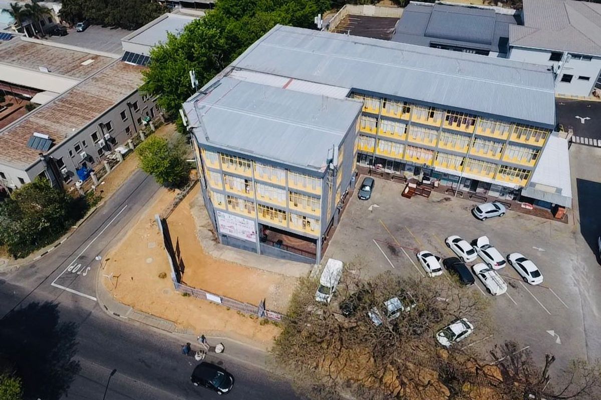 Aerial view of a multi-story commercial building featuring a metal roof, paved parking area, and perimeter fencing in an urban setting.