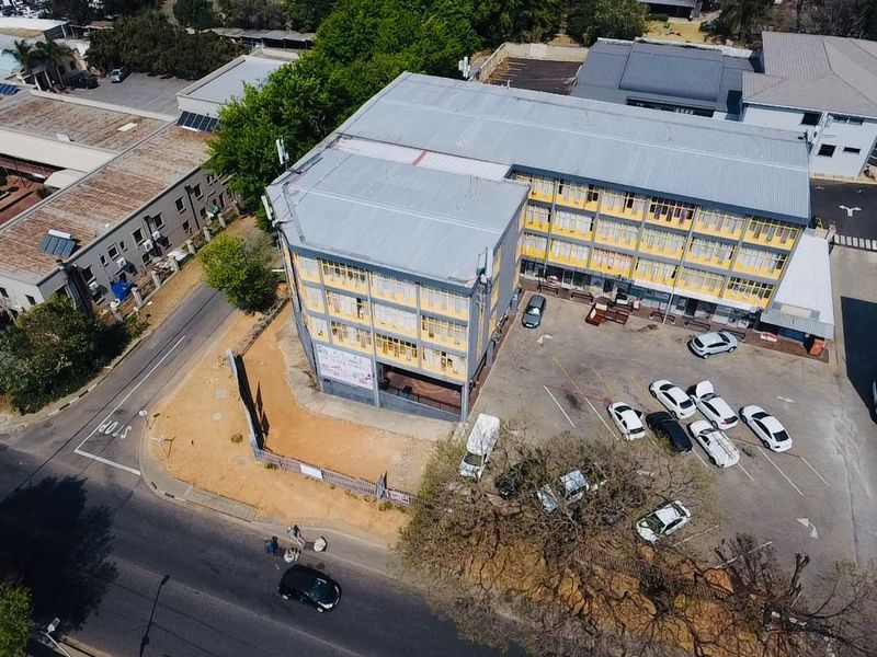 Aerial view of a multi-story commercial building featuring a metal roof, paved parking area, and perimeter fencing in an urban setting.