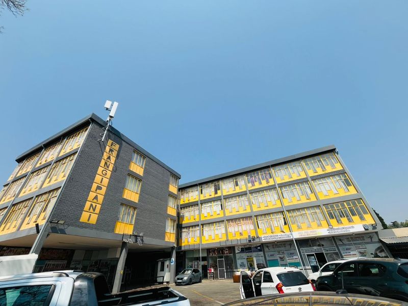 A multi-story commercial building featuring a yellow and grey facade with large windows and an integrated ground-level parking area.