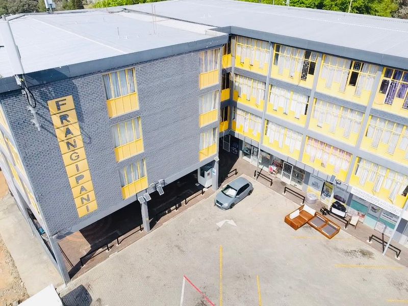 Aerial view of a multi-story commercial building featuring a paved parking courtyard and distinctive yellow and grey exterior facade.
