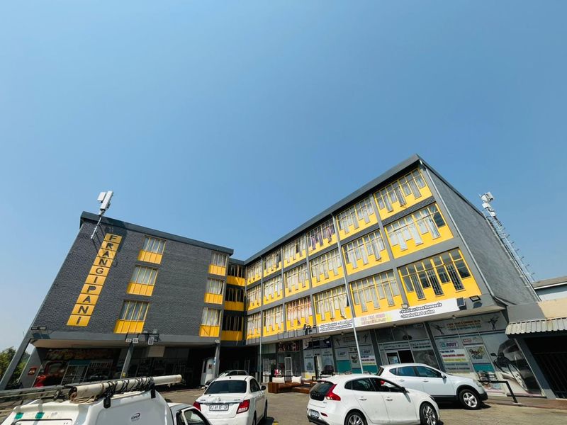A multi-story commercial building facade featuring yellow and grey exterior finishes with large windows and ground-level retail or workshop access.