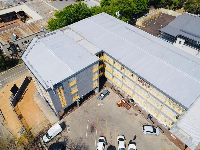 Aerial view of a multi-story commercial building featuring a metal roof and an adjacent asphalt parking area.