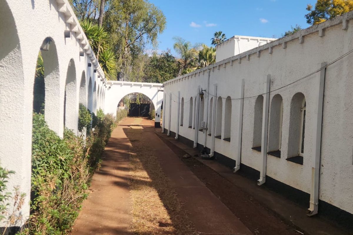 A long exterior walkway featuring a distinctive arched colonnade and white stucco walls with arched windows, leading towards the rear of the farm property.