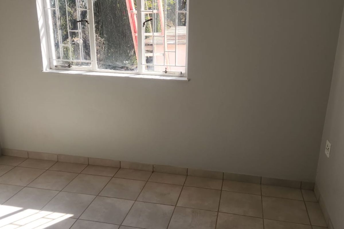 A clean, empty bedroom featuring neutral tiled flooring and a window fitted with security bars, offering a blank canvas for personalization.