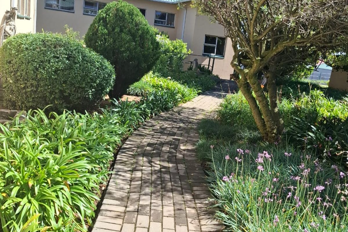A well-maintained paved garden path leading alongside the building exterior, featuring established greenery and mature landscaping.