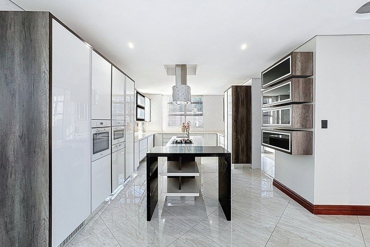 Modern, spacious kitchen featuring high-gloss cabinetry, a central island with integrated hob, built-in appliances, and polished tiled flooring.