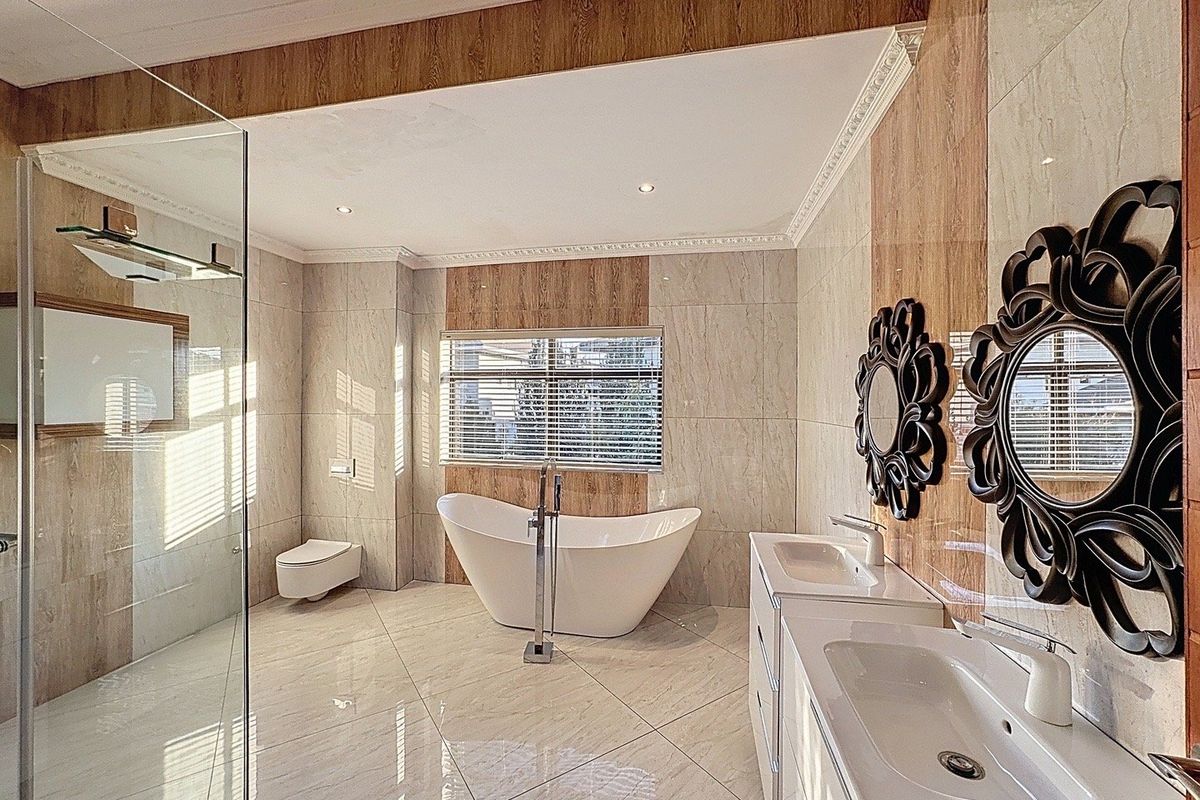 Modern, spacious bathroom featuring a freestanding bathtub, double vanity, wall-mounted toilet, and a large glass-enclosed shower with elegant floor-to-ceiling tiling.
