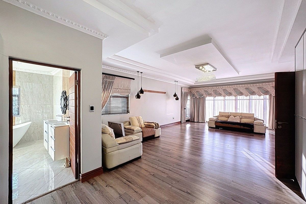 Spacious living area featuring laminate flooring, recessed ceiling with crown molding, and direct access to an adjoining bathroom with a modern vanity and bathtub.
