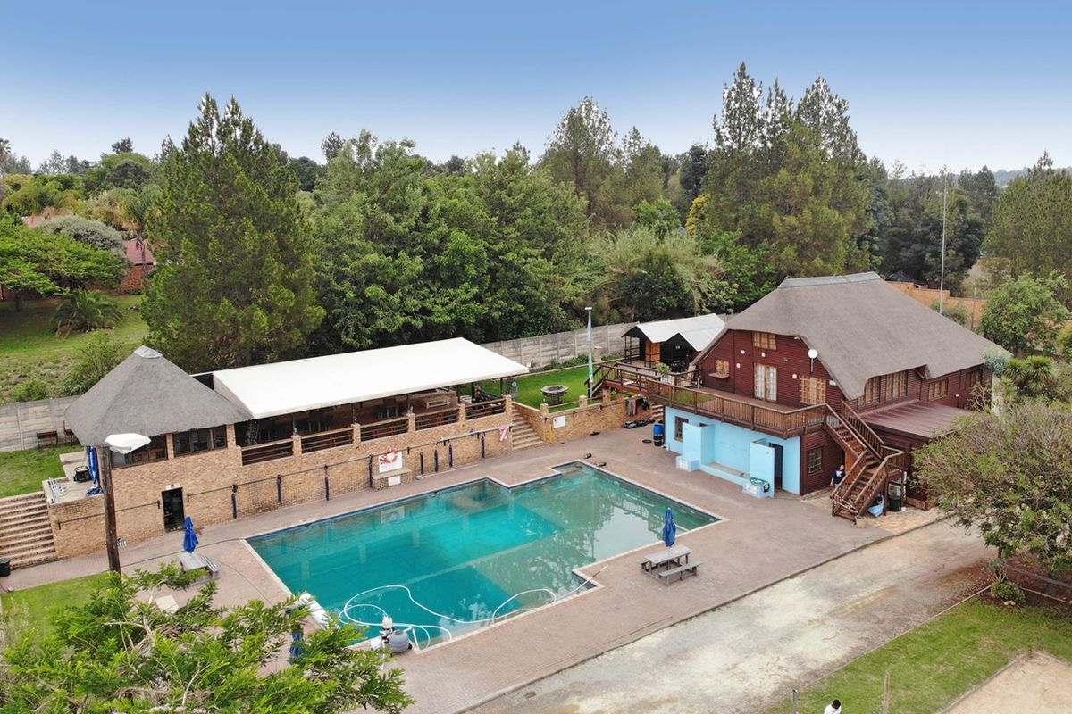 Aerial view of a commercial property featuring a large swimming pool, thatched roof structures, covered patio area, and extensive outdoor grounds.