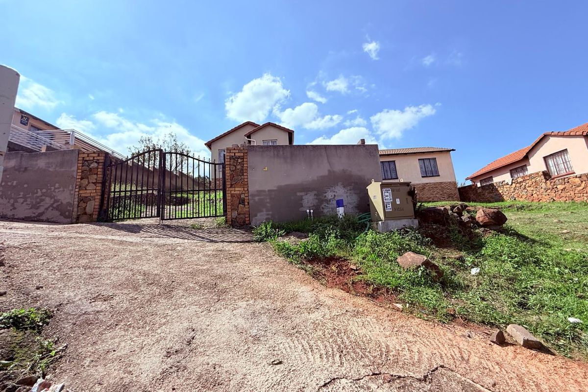 Exterior view of the property entrance featuring a metal gate, boundary wall, and concrete driveway leading to the residential structure.