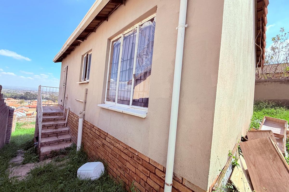 Exterior view of the property side elevation featuring brick base, plastered walls, and external staircase leading to an elevated entrance.