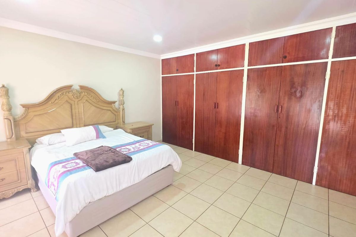 Spacious bedroom featuring extensive floor-to-ceiling built-in wooden cupboards and neutral tiled flooring throughout.