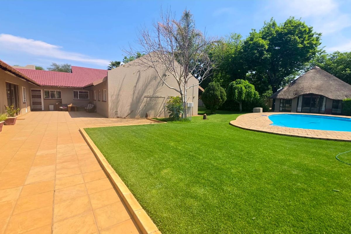 Spacious rear garden featuring a paved patio area, a well-maintained lawn, and a swimming pool with an adjacent thatched lapa.