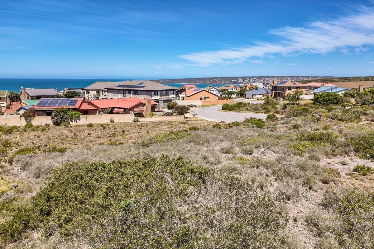 An elevated aerial view of a vacant residential plot overlooking a coastal neighborhood and the ocean in the distance.
