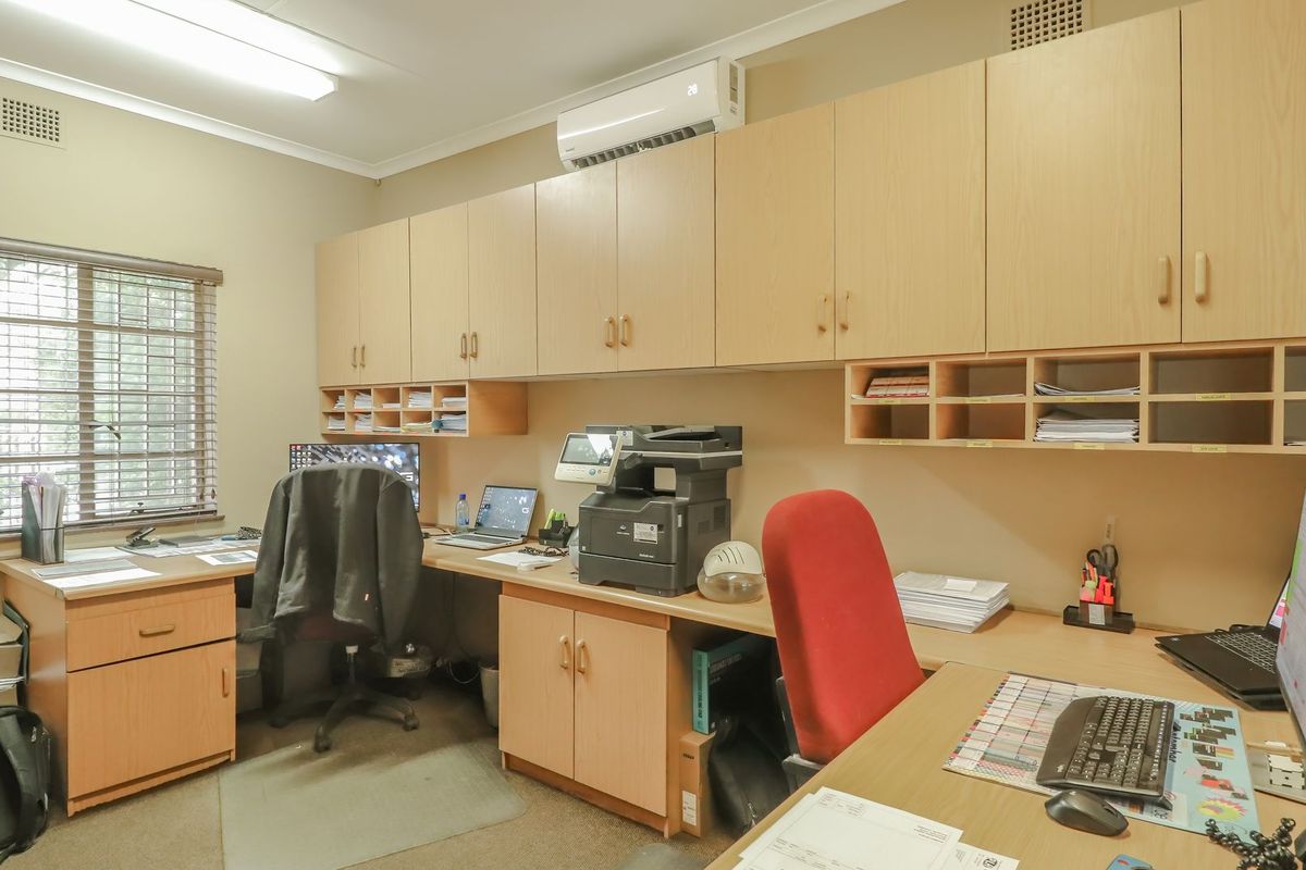A functional commercial office space featuring extensive built-in cabinetry, integrated desk workstations, and a wall-mounted air conditioning unit.