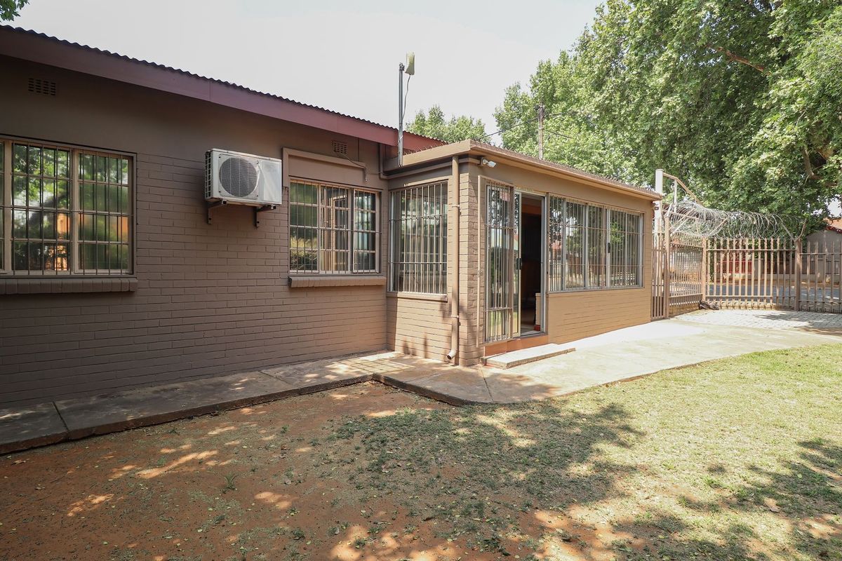 Rear exterior view of a commercial building featuring brick walls, security bars on windows, an air conditioning unit, and a paved walkway.