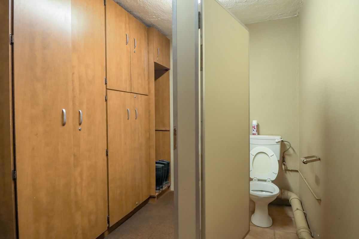 A functional commercial bathroom featuring built-in storage cabinetry and a standard toilet with exposed plumbing fixtures.