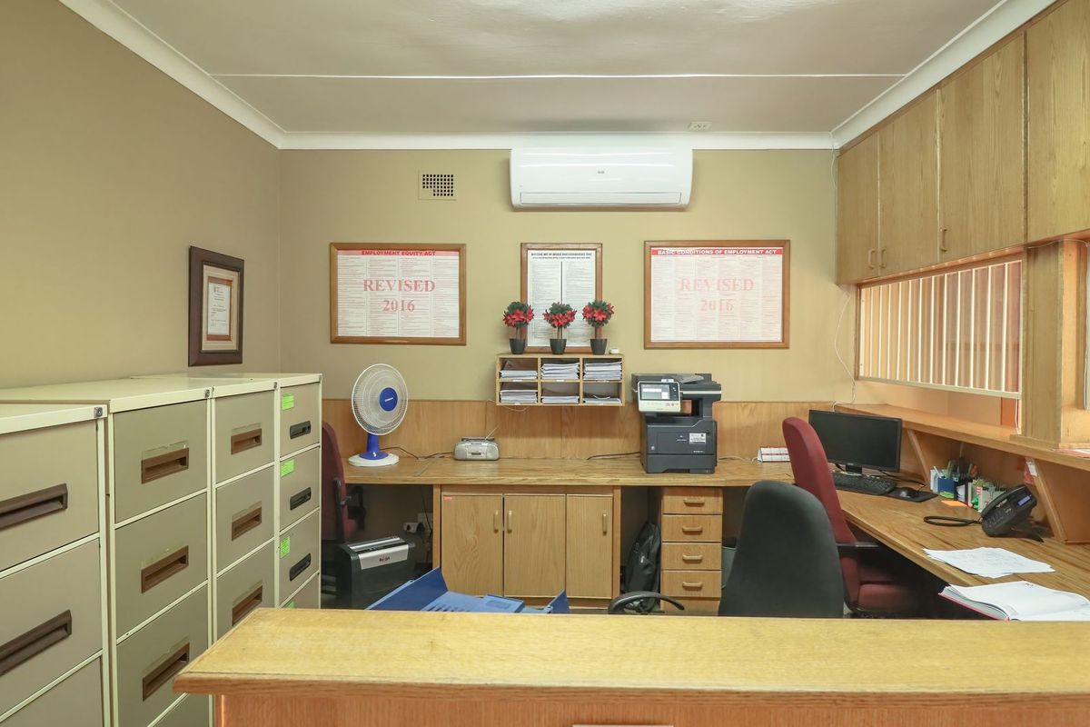 A functional commercial office space featuring built-in wooden cabinetry, integrated desk workstations, and a wall-mounted air conditioning unit.