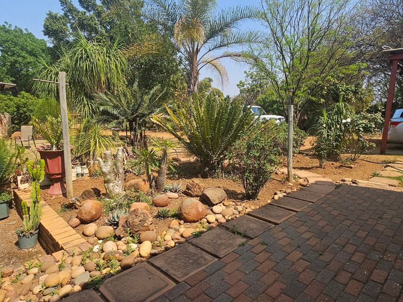 Spacious garden area featuring a brick-paved patio, a built-in brick braai, and a covered carport, offering a functional outdoor entertainment space.