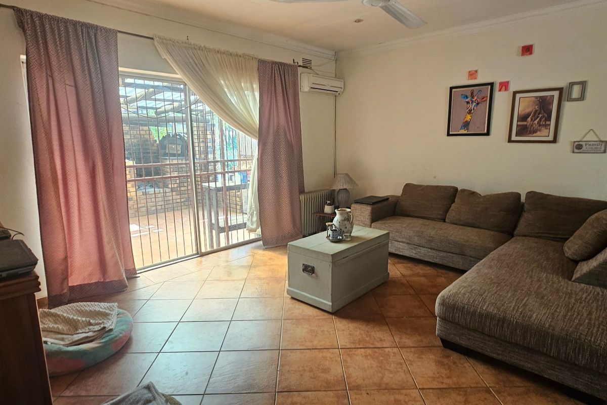 A comfortable living room featuring tiled flooring, a ceiling fan, wall-mounted air conditioning, and direct access to an outdoor patio area through sliding glass doors.