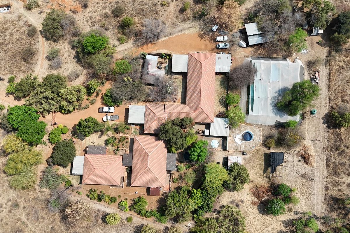 Aerial view of a residential property featuring multiple tiled roof structures, a swimming pool, and surrounding landscaped grounds.