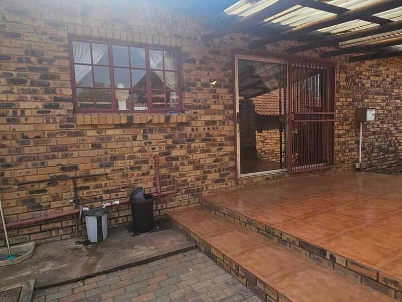 A covered outdoor patio area featuring tiled flooring, face brick walls, and a sliding door entrance, providing a functional space for outdoor living.