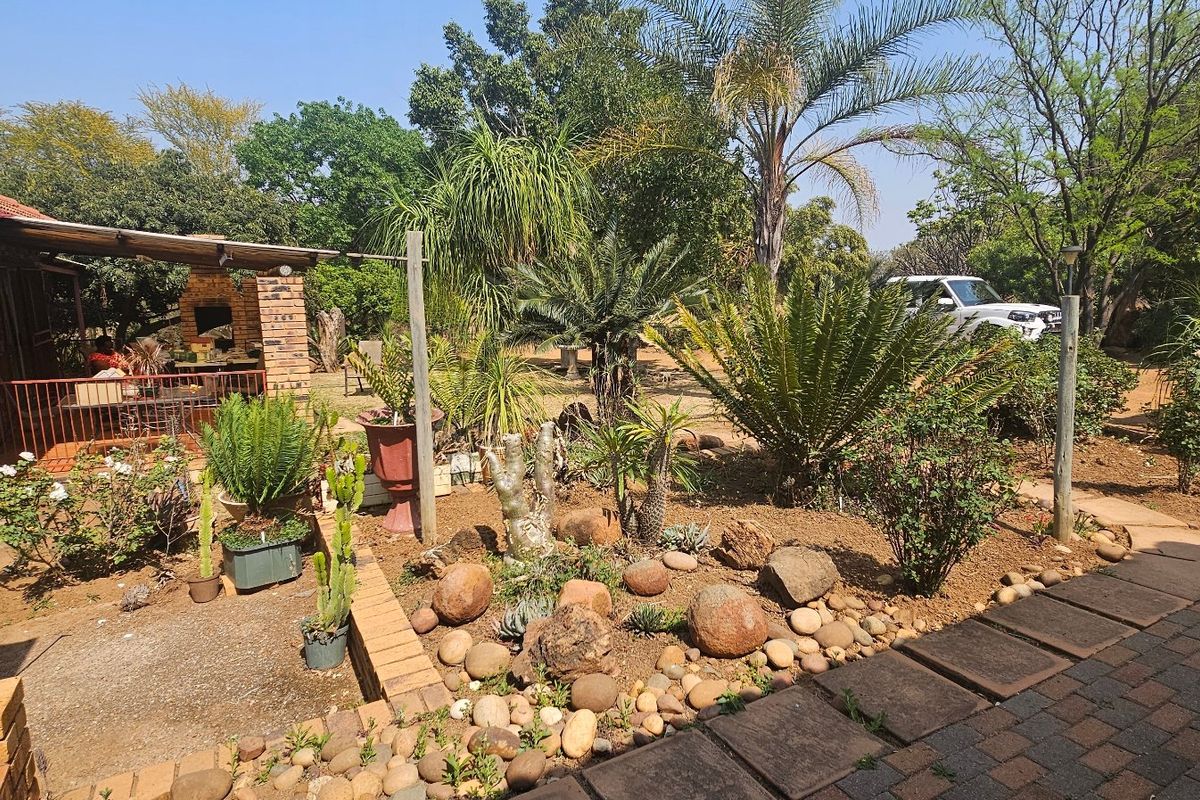 A rear exterior view featuring a brick house facade, a covered patio area with a built-in braai, and a landscaped garden with paved pathways.