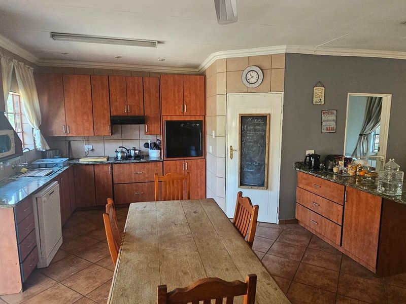 Open-plan kitchen and dining area featuring wooden cabinetry, granite countertops, built-in oven, and tiled flooring, offering a functional layout for family living.