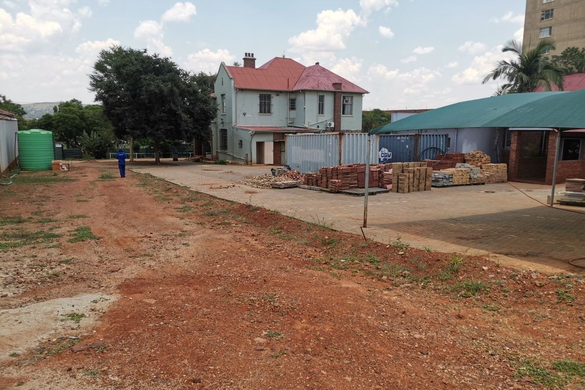 Rear view of the property showing a large unpaved yard area, paved driveway section, water tank, and a shade cloth structure.