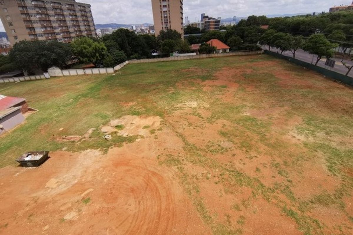 An aerial view of a large, vacant residential plot featuring open grass and soil areas, enclosed by perimeter fencing in an urban setting.